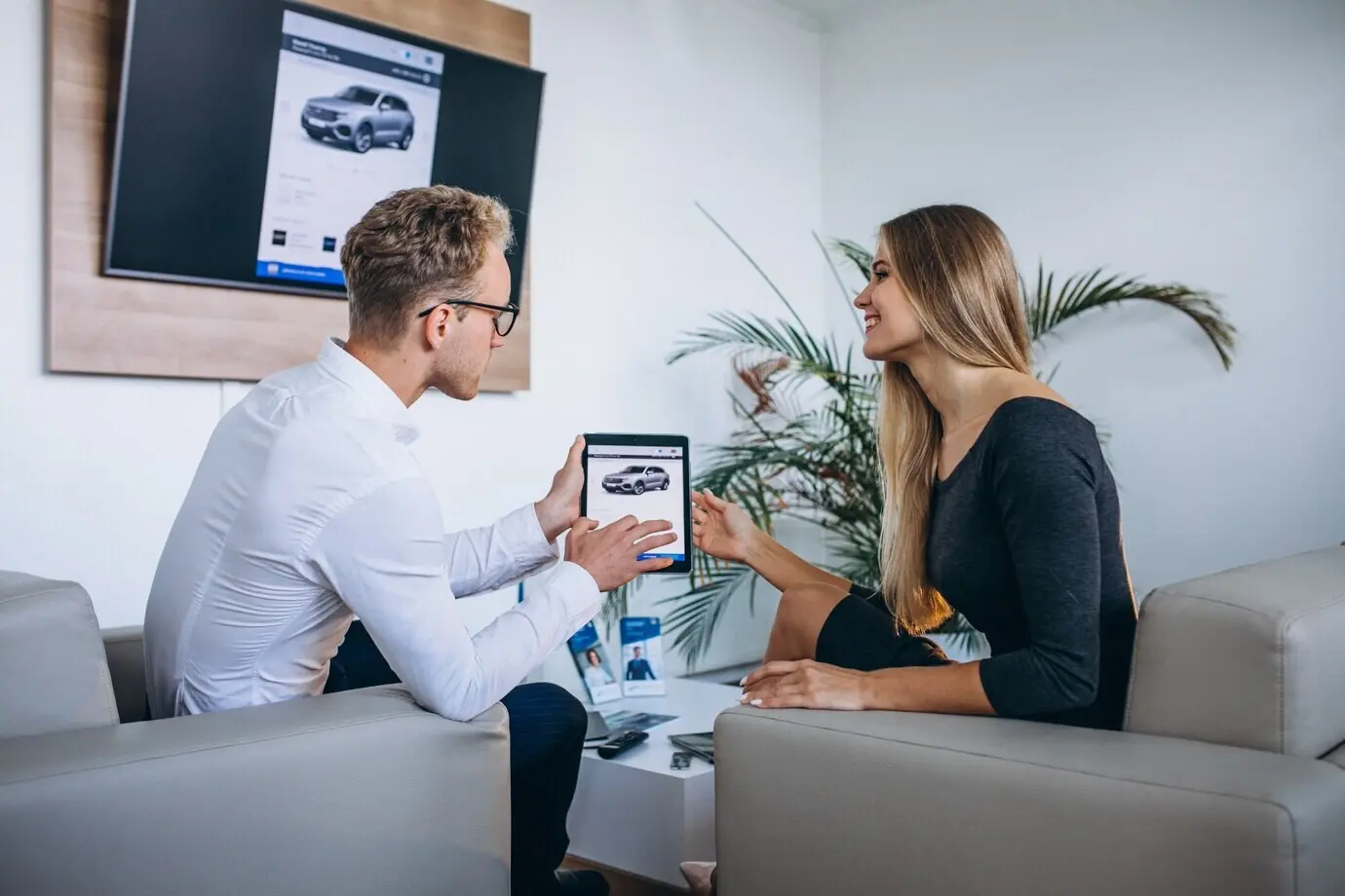 Un homme et une femme utilisent une tablette dans un showroom automobile.