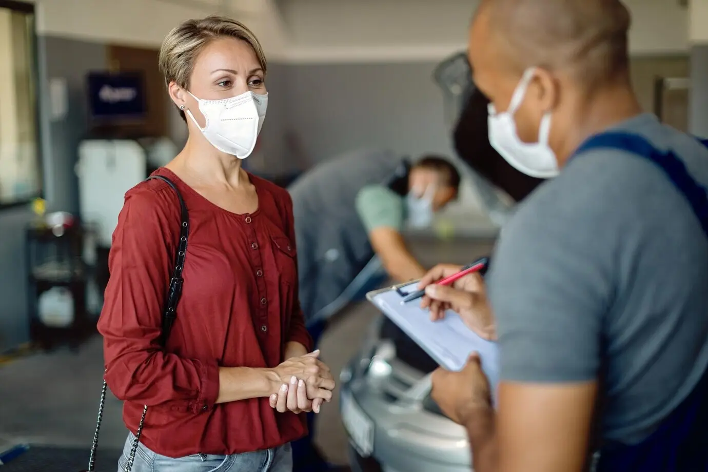 Une femme portant un masque parle avec un mécanicien automobile dans un atelier.